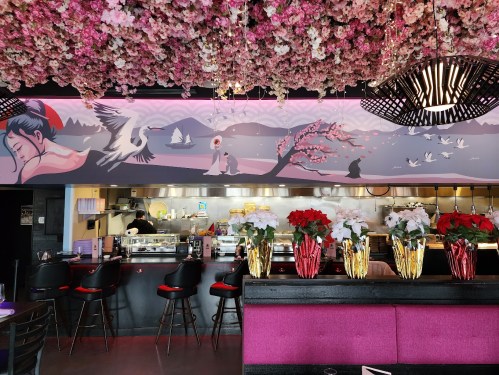 A vibrant restaurant interior featuring floral decor, a mural of serene landscapes, and a bar with festive plants.