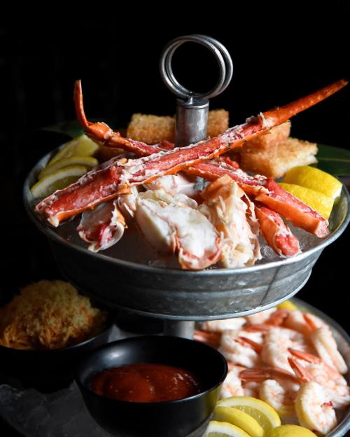 A tiered seafood platter featuring crab legs, shrimp, lemon slices, and dipping sauce, elegantly presented.