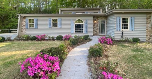 a cozy home with a sidewalk path leading up to the front door and pink flower bushes surrounding it