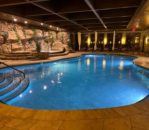 Indoor pool with a waterfall feature, surrounded by lounge chairs and soft lighting. Relaxing atmosphere.