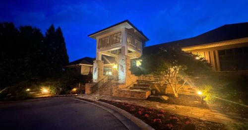 A beautifully lit entrance of a house at night, featuring stone steps and landscaped gardens.