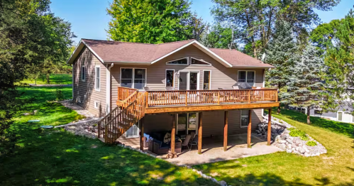 Exterior of a two-story lakeside Airbnb in Parkers Prairie, MN, featuring a large wooden sun deck and green lawn.