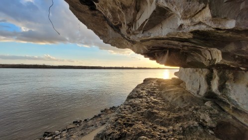 A serene riverside view with rocky cliffs and a sunset reflecting on the water.