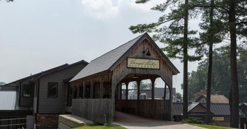 A rustic restaurant with a peaked roof and wooden exterior, surrounded by trees and a clear sky.