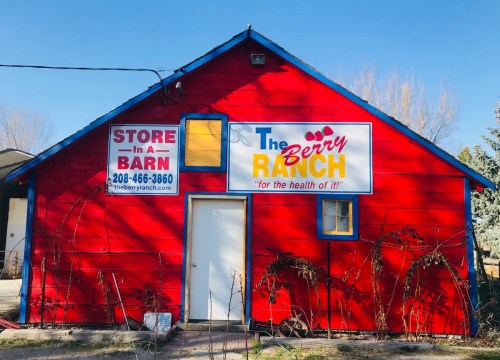 A bright red barn with signs for "The Berry Ranch" and a phone number, set against a clear blue sky.