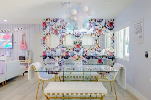 A stylish dining area with a glass table, gold accents, and a colorful photo wall featuring round mirrors.