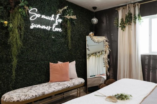 A cozy room with a green wall, a neon sign, a mirror, and soft furnishings, creating a warm, inviting atmosphere.