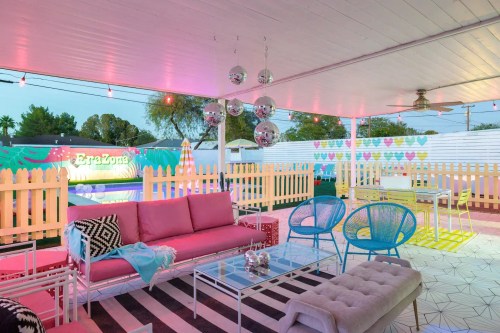 Colorful outdoor lounge area with pink sofas, blue chairs, and decorative lights, creating a vibrant atmosphere.