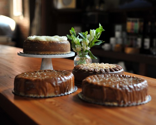 Four beautifully decorated cakes on a wooden table, with a small vase of flowers in the background.