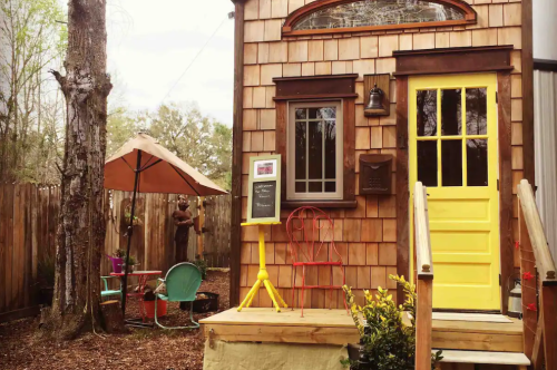 A cozy wooden building with a yellow door, outdoor seating, and a welcoming atmosphere in a garden setting.