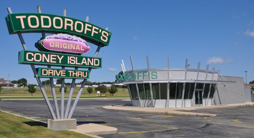 Sign for Todoroff's Original Coney Island Drive-Thru with a modern building and clear blue sky in the background.