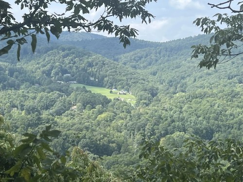 Lush green mountains and valleys under a cloudy sky, framed by tree branches in the foreground.