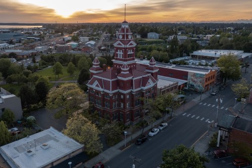 Aerial view of a historic red brick building at sunset, surrounded by greenery and cityscape.