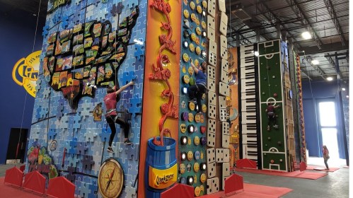 Indoor climbing gym featuring colorful climbing walls with various themes, including a map of the USA and a piano.