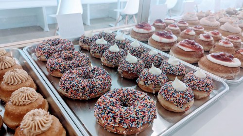 A display of colorful donuts with sprinkles and cream, alongside other pastries topped with fruit and frosting.