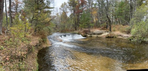 A serene river scene with gentle waterfalls, surrounded by autumn foliage and lush greenery.