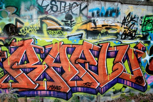Colorful graffiti featuring bold lettering in orange and purple against a vibrant, multi-colored background.