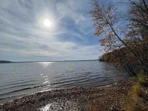 A serene lakeside view with sunlight reflecting on the water, surrounded by trees and autumn foliage.