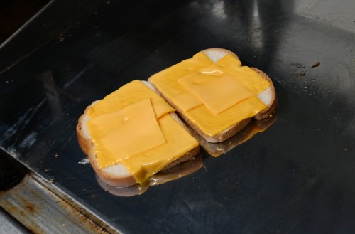 Two slices of bread with melted cheese on a griddle, ready for a sandwich.