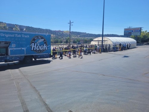 A food truck named "On the Hook" with a long line of people waiting outside in a sunny parking lot.