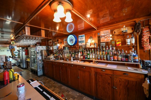 A wooden bar with a variety of liquor bottles, glasses hanging above, and a cozy, warm atmosphere.