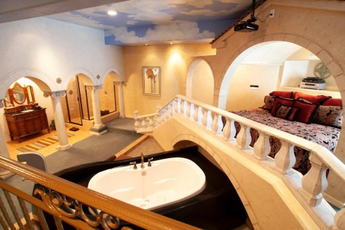 A spacious room featuring a large bed, a jacuzzi tub, and elegant architectural details with arches and soft lighting.