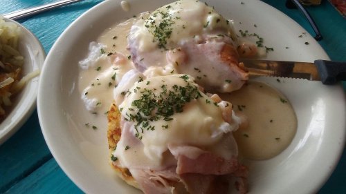 A plate of eggs Benedict with ham, topped with hollandaise sauce and parsley, served on a toasted English muffin.