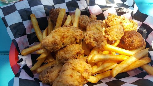 A basket of golden fried chicken pieces and crispy French fries on a checkered paper liner.