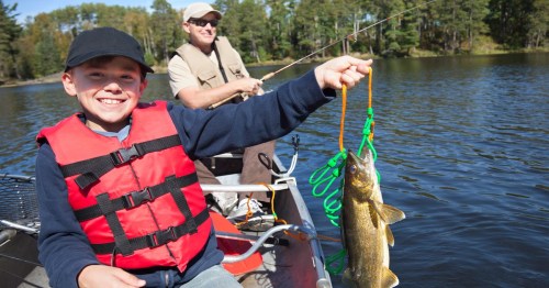 Smiling boy fisherman in a canoe holds up a stringer with nice walleyes, Lake Eau Claire, Wisconsin.