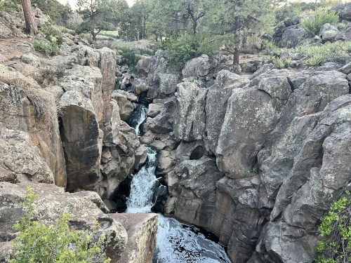 A rocky canyon with a flowing waterfall surrounded by trees and vegetation.