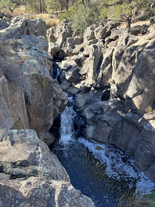 A serene waterfall cascades through rocky cliffs, surrounded by trees and natural vegetation.