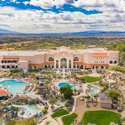 Aerial view of a resort with pools, water slides, and lush landscaping under a partly cloudy sky.