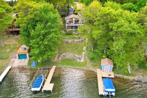Aerial view of a lakeside property with a house, docks, and lush green trees surrounding the water.