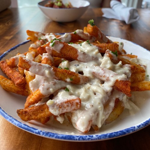 A plate of crispy fries topped with creamy sauce and sprinkled with herbs, served on a wooden table.