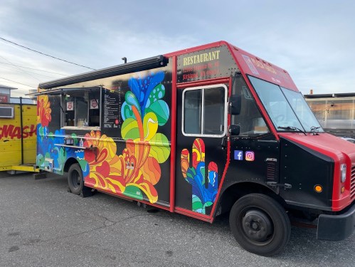 A colorful food truck with vibrant designs parked in an outdoor area, featuring a menu on the side.