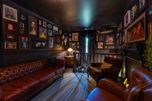 Cozy room with dark walls, vintage art, a leather sofa, and a warm lamp, creating an inviting atmosphere.