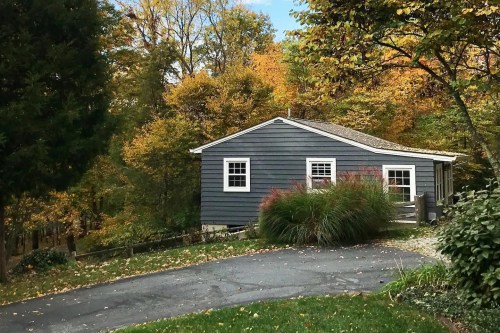 A cozy gray house surrounded by vibrant autumn foliage and a winding driveway.