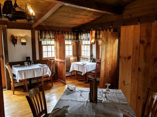Cozy wooden dining room with tables set for guests, featuring warm lighting and rustic decor.