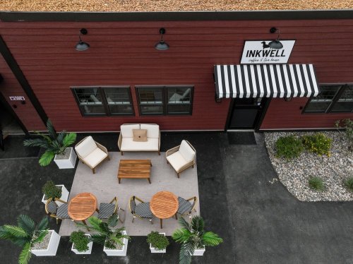 Aerial view of INK WELL café with outdoor seating, potted plants, and a striped awning on a red building.