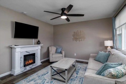 Cozy living room with a fireplace, modern furniture, a ceiling fan, and a large TV on the wall.