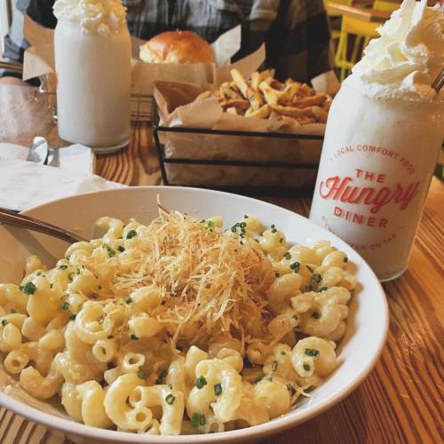 A bowl of creamy macaroni and cheese topped with crispy onions, with a milkshake and fries in the background.