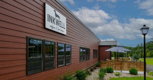 Exterior of Inkwell Coffee & Tea House, featuring a wooden facade, patio umbrellas, and landscaped greenery.
