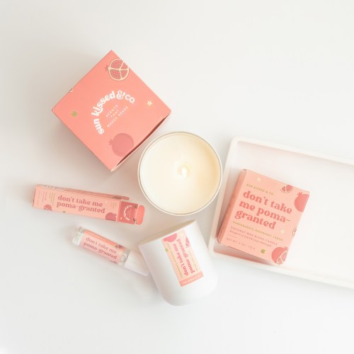 A flat lay of skincare products and a candle, all in pink packaging with playful designs and text.