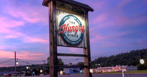 Sign for "The Hungry Diner" with a colorful sunset in the background, featuring local food and craft beer.