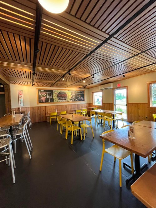 Interior of a restaurant featuring wooden walls, yellow chairs, and a chalkboard menu. Bright and spacious atmosphere.