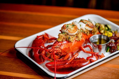 A beautifully presented lobster dish topped with scallops and served with a side of vegetables and dipping sauce.