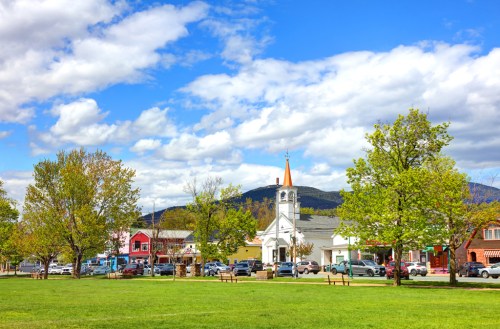 A scenic view of a small town with a church steeple, colorful buildings, trees, and a blue sky with clouds.