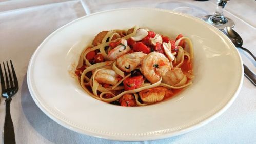 A plate of linguine pasta topped with shrimp, scallops, and diced tomatoes in a light sauce.