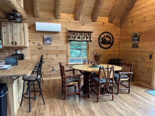 Cozy wooden cabin interior featuring a dining table, chairs, and rustic decor with large windows and log walls.