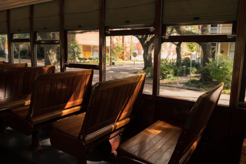 Interior of a vintage bus with wooden benches, sunlight streaming through the windows, and a view of a quiet street outside.